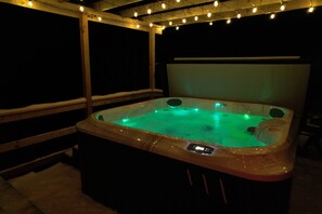 Ein Whirlpool mit Bedienfeld, umgeben von einer Holzterrasse und Lichterketten.
