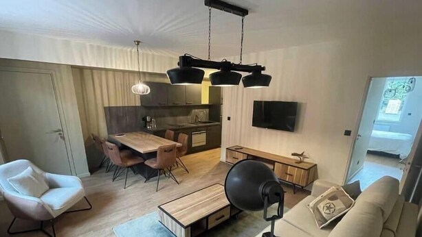 A modern living room with a sofa, a dining table with chairs, a kitchen area, and a TV mounted on the wall. - Appart ' Hôtel "Pilote" - 4/6 Pers (Niergnies)