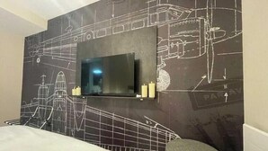 A bedroom with a bed, a TV mounted on the wall, and a small seating area. - Appart ' Hôtel "Pilote" - 4/6 Pers (Niergnies)