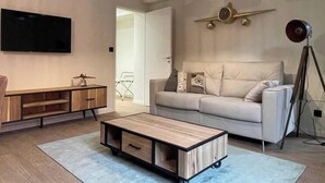 A modern living room with a sofa, a coffee table with drawers, a TV, and a decorative clock. - Appart ' Hôtel "Pilote" - 4/6 Pers (Niergnies)