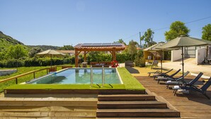 A swimming pool with a wooden deck, lounge chairs, and a pergola with solar panels.