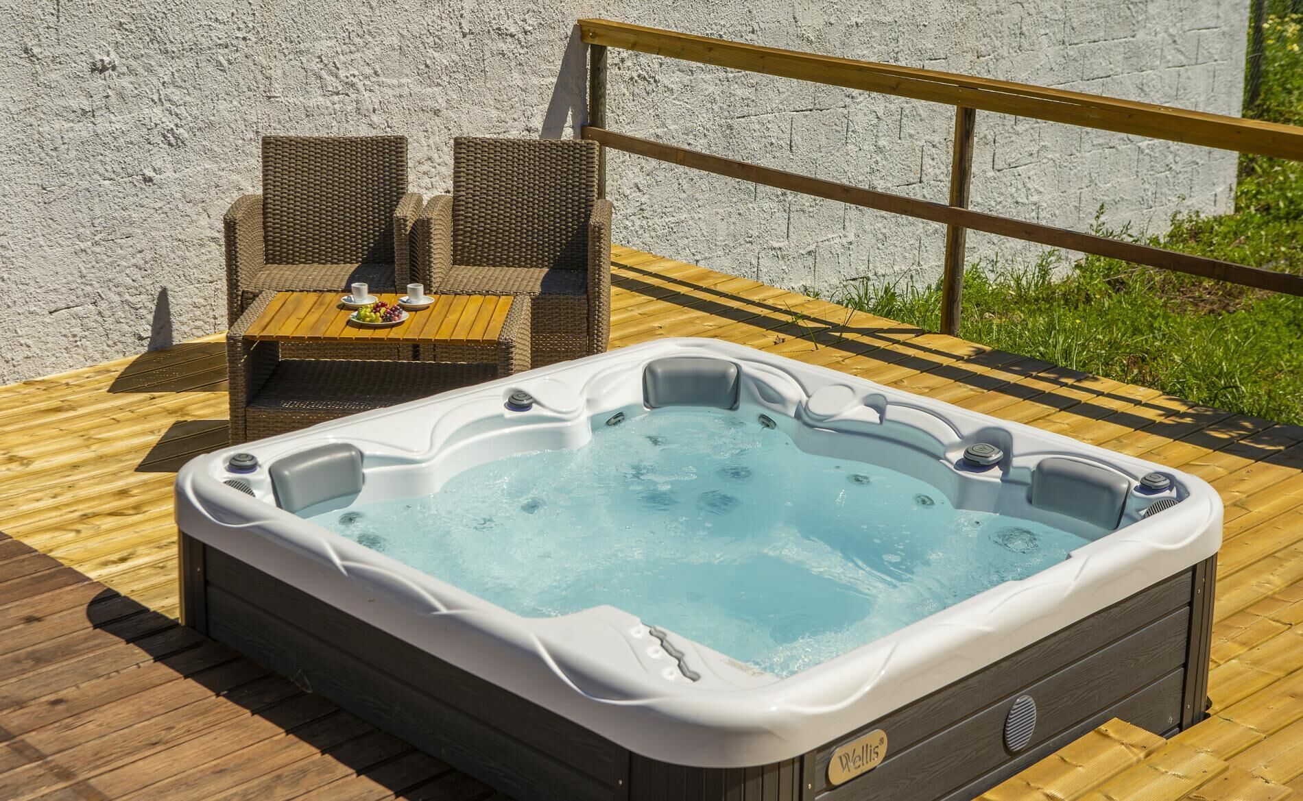 Un bain à remous sur une terrasse en bois, avec des fauteuils en osier et une table garnie de fruits.