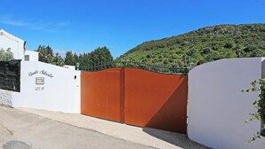 A gated property with a white wall and a brown gate, surrounded by a hilly landscape.