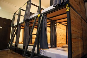 A bunk bed room with wooden walls and metal frames, numbered beds, and curtains.