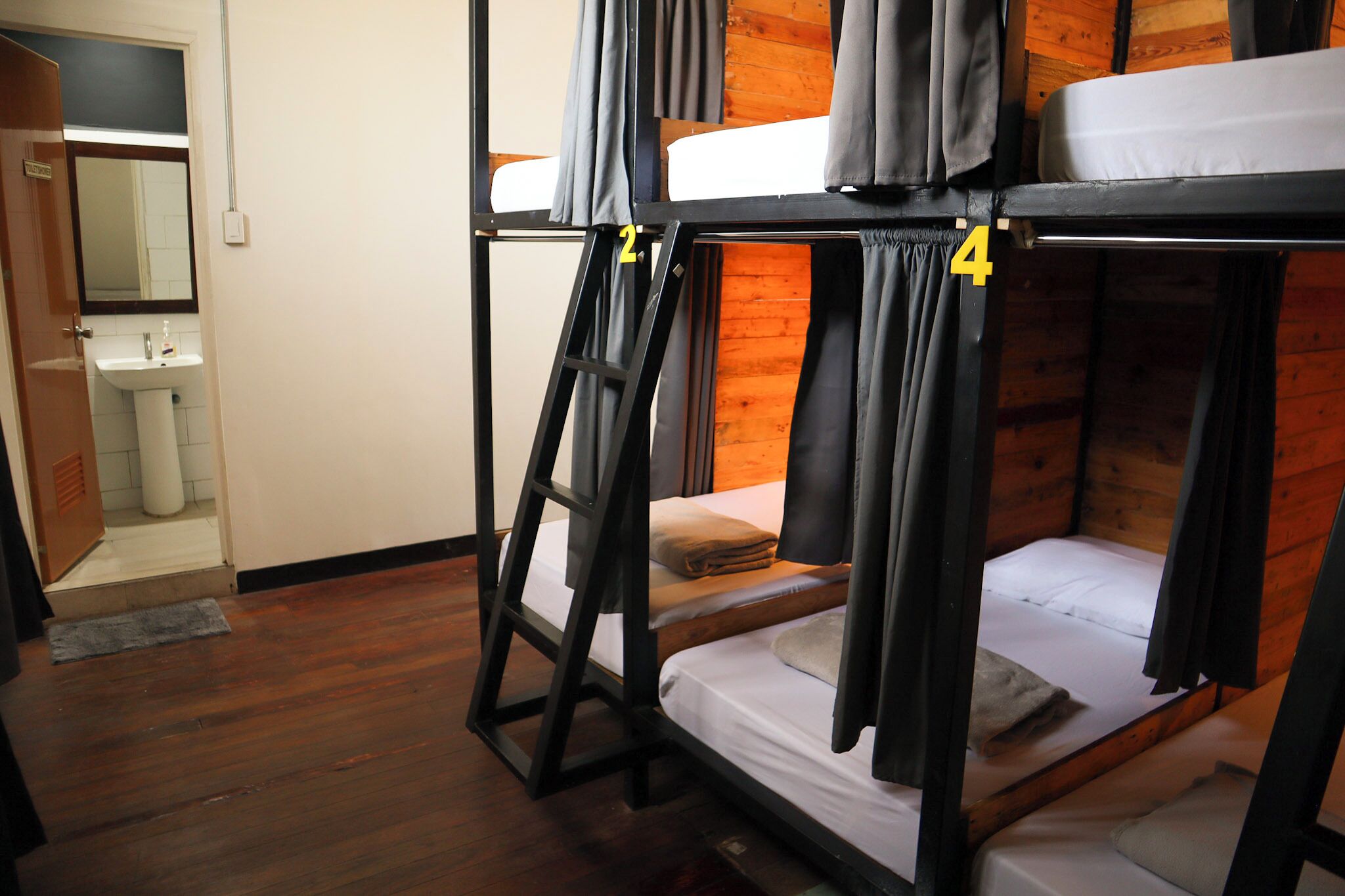 Habitación con literas, suelo de madera, un lavamanos y un espejo en la esquina.