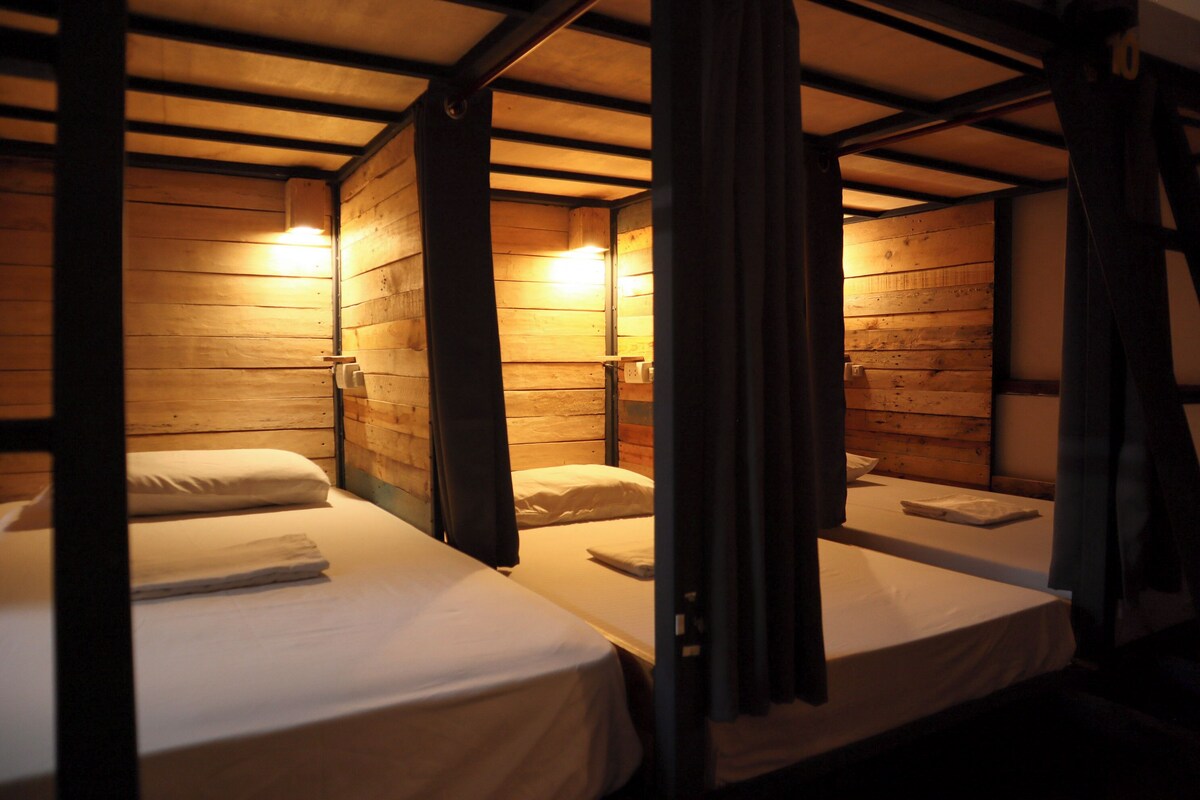 A room with three wooden bunk beds, each with a white mattress and a folded towel.