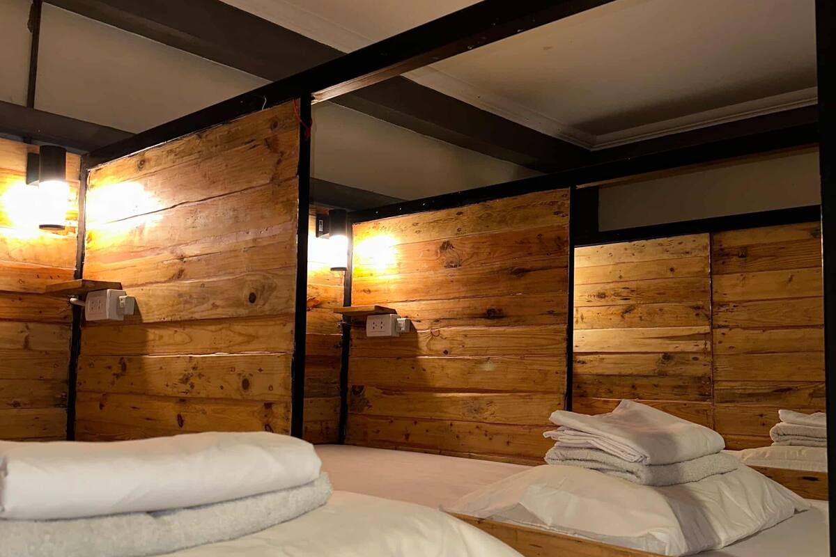 Ein Zimmer mit Holzwänden, Metallbalken und Betten mit weißen Leinenbezügen.