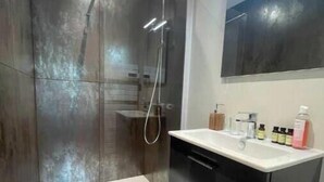 Een moderne badkamer met een ruime douche, een grote spiegel en een wastafelmeubel met een wastafel.