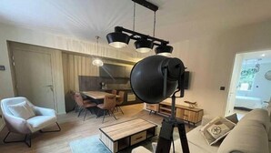 Een moderne woonkamer met een witte bank, een eethoek met een houten tafel en stoelen, en een keuken op de achtergrond.