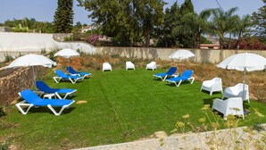 A well-maintained outdoor area with multiple lounge chairs and umbrellas, surrounded by a stone wall and greenery. - X 06 - 1 Bed Apartment in Quinta da Ponte (Lagos)