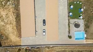 An aerial view of a property with two large parking areas, a swimming pool, and a small garden with lounge chairs. - X 06 - 1 Bed Apartment in Quinta da Ponte (Lagos)