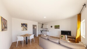 A modern living room with a sofa, dining table, chairs, a TV, and artwork on the walls. - X 06 - 1 Bed Apartment in Quinta da Ponte (Lagos)