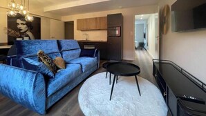 A modern living room with a blue sofa, a white round rug, a black coffee table, and a kitchen in the background. - Suite "Art Déco" - 2/4 Pers (Niergnies)