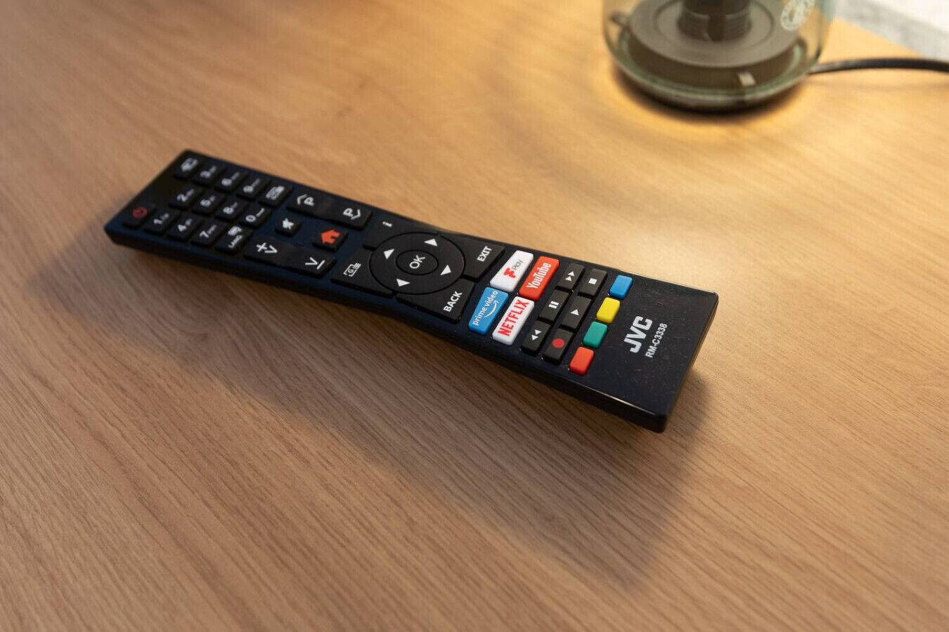 A black remote control with buttons for Netflix, Hulu, and other functions on a wooden surface.