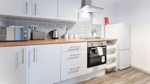 Une cuisine moderne avec des meubles blancs, un four encastré, un four à micro-ondes et une bouilloire.