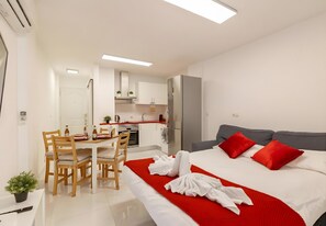 Ein modernes Hotelzimmer mit Bett, Esstisch mit Stühlen, Küchenzeile und kleinem Balkon.