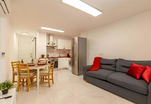 Ein moderner Wohnraum mit Essbereich, Küche und einem grauen Sofa mit roten Kissen.