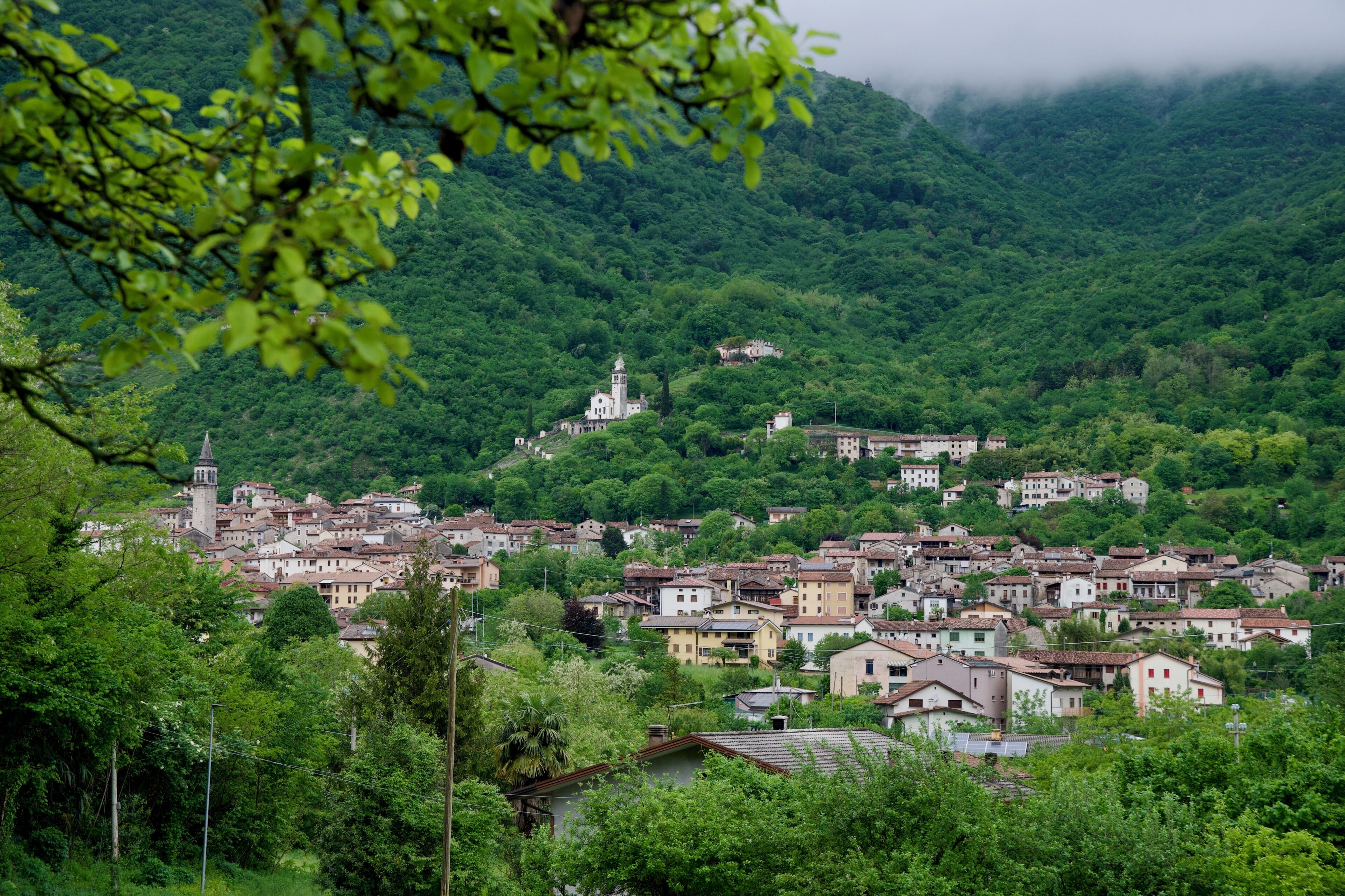 A hillside village with traditional buildings, a church with a bell tower, and lush greenery.