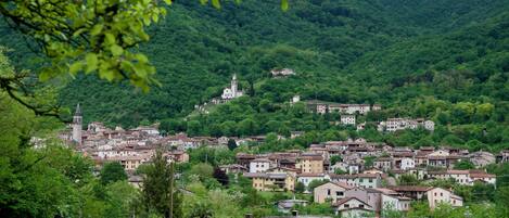 A hillside village with traditional buildings, a church with a bell tower, and lush greenery.