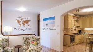 A living room with floral armchairs, a small round table, a world map wall art, and a kitchen with light-colored cabinets. - Happy Corner - The Home for Outdoor Lovers - (Veneto)