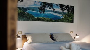 A bedroom with a bed, two bedside lamps, a neatly made bed with towels, and a large landscape painting on the wall. - Happy Corner - The Home for Outdoor Lovers - (Veneto)
