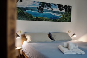 Quarto com cama, duas luminárias de cabeceira, cama bem arrumada com toalhas e uma grande pintura de paisagem na parede.
