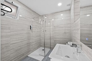 Un baño moderno con cabina de ducha de vidrio, un lavabo blanco y un espejo.