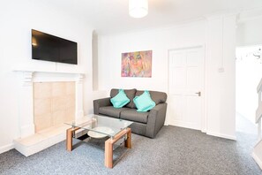 A living room with a fireplace, a sofa, a coffee table, and a flat-screen TV mounted on the wall. - City Centre • Parking • TVs • Ideal for Work Crew (Swansea)