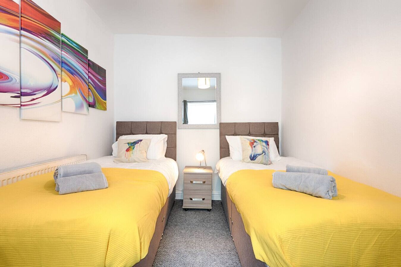 Ein Hotelzimmer mit zwei Betten, einem Nachttisch, einem Spiegel und einem farbenfrohen, abstrakten Gemälde an der Wand.