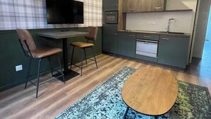 Una cocina compacta con televisor de pantalla plana, dos sillas, una pequeña mesa de comedor y un tapete estampado.