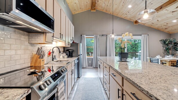 Une cuisine moderne dotée d’un grand îlot central, d’appareils électroménagers en acier inoxydable et d’un plafond en bois.