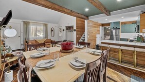 A dining area with a wooden table set for four, a red pot, and a kitchen with wooden cabinets and a refrigerator. - Dog Friendly Cabin w Hot Tub Sauna Fire Pit (Tobyhanna)