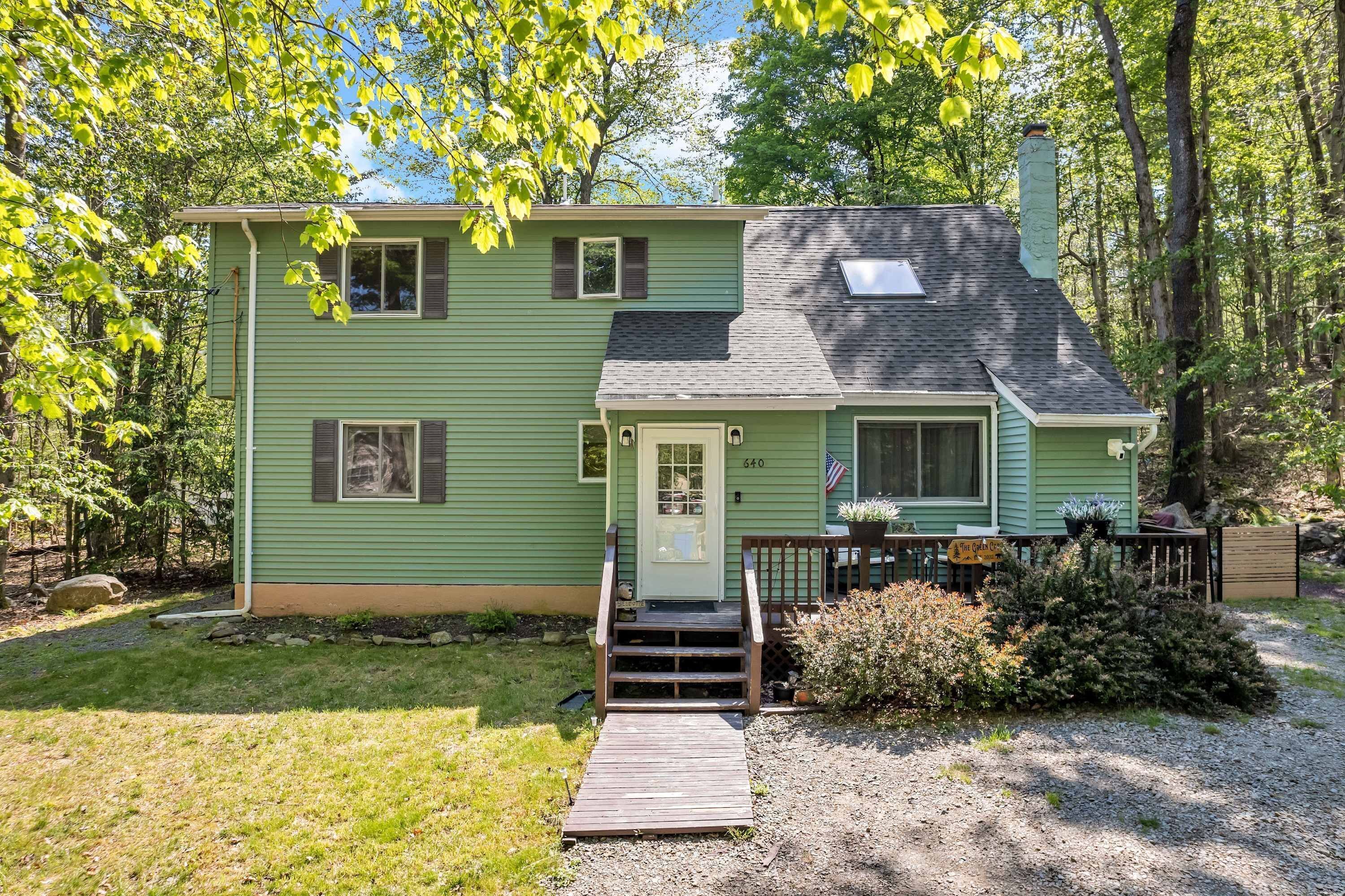A green house with a front porch, a chimney, and a small deck.