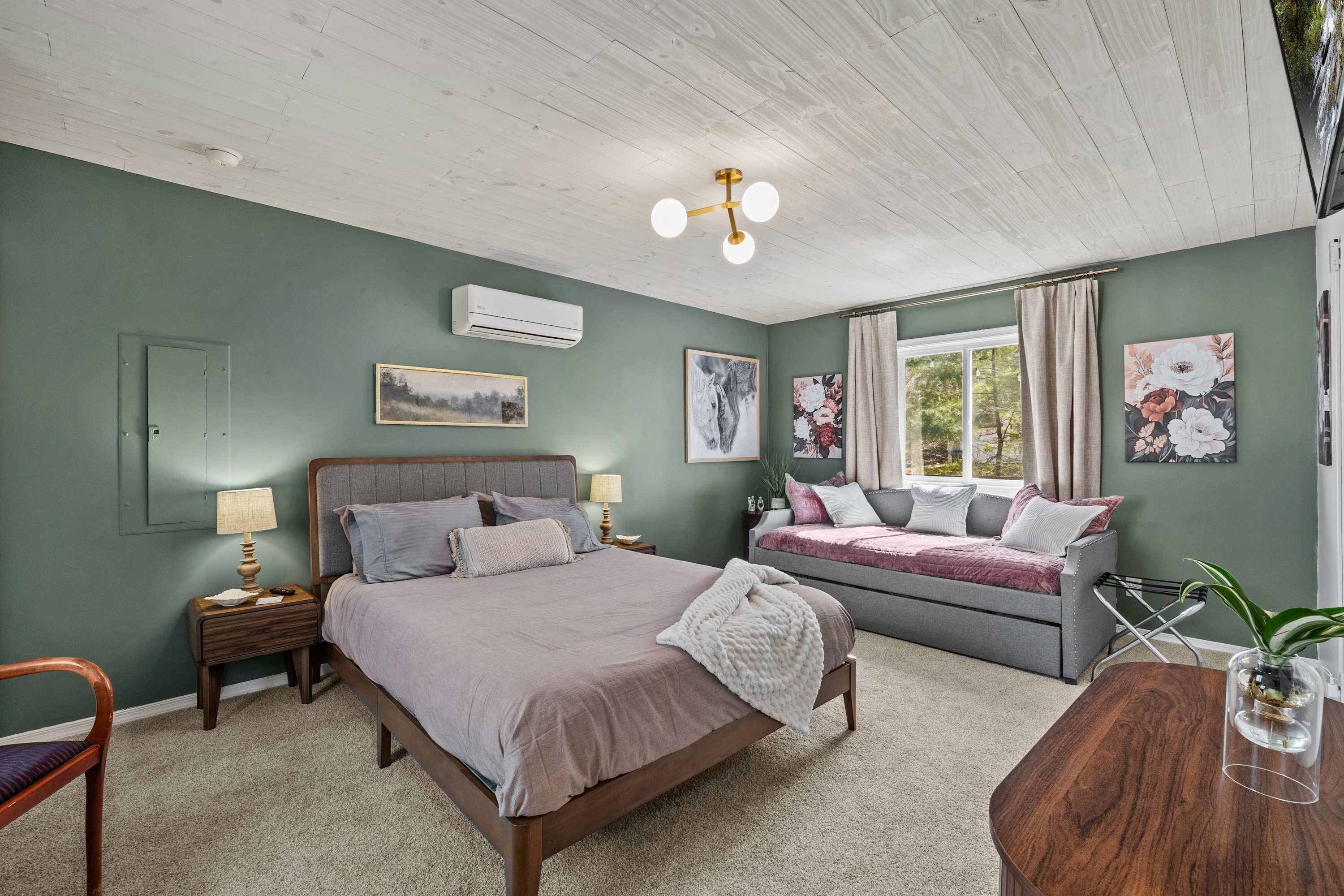Un dormitorio con una cama, un sofá, una mesita de madera, una silla y una ventana con cortinas.