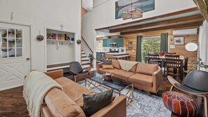 A spacious living area with a sofa, coffee table, and a dining area with chairs and a table. - Dog Friendly Cabin w Hot Tub Sauna Fire Pit (Tobyhanna)