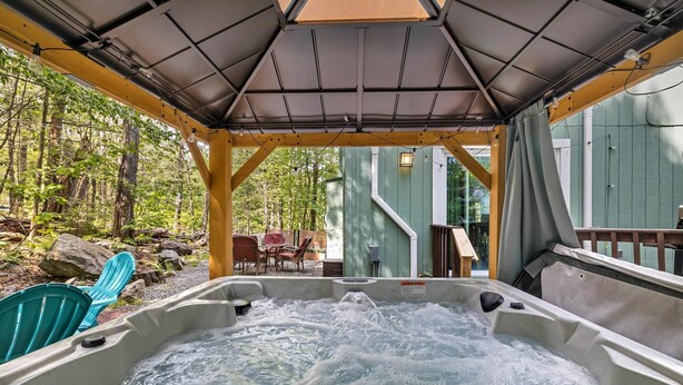 A hot tub with a wooden deck and a covered area, surrounded by greenery and a wooden deck. - Dog Friendly Cabin w Hot Tub Sauna Fire Pit (Tobyhanna)