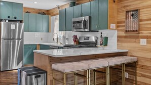A kitchen with teal cabinets, stainless steel appliances, a marble island, and a bench. - Dog Friendly Cabin w Hot Tub Sauna Fire Pit (Tobyhanna)