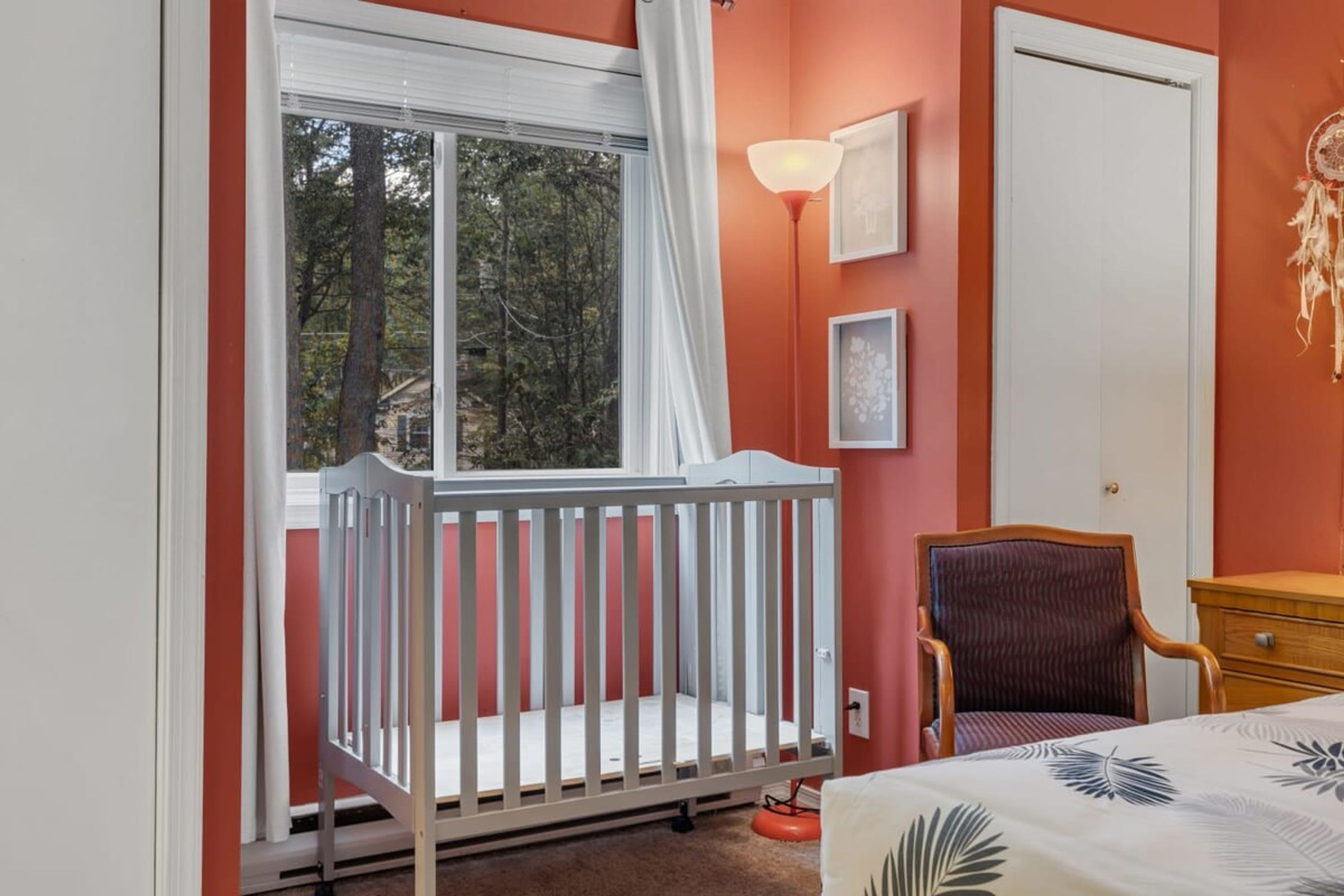 A room with a crib, a chair, a bed, a dresser, and a window with curtains.