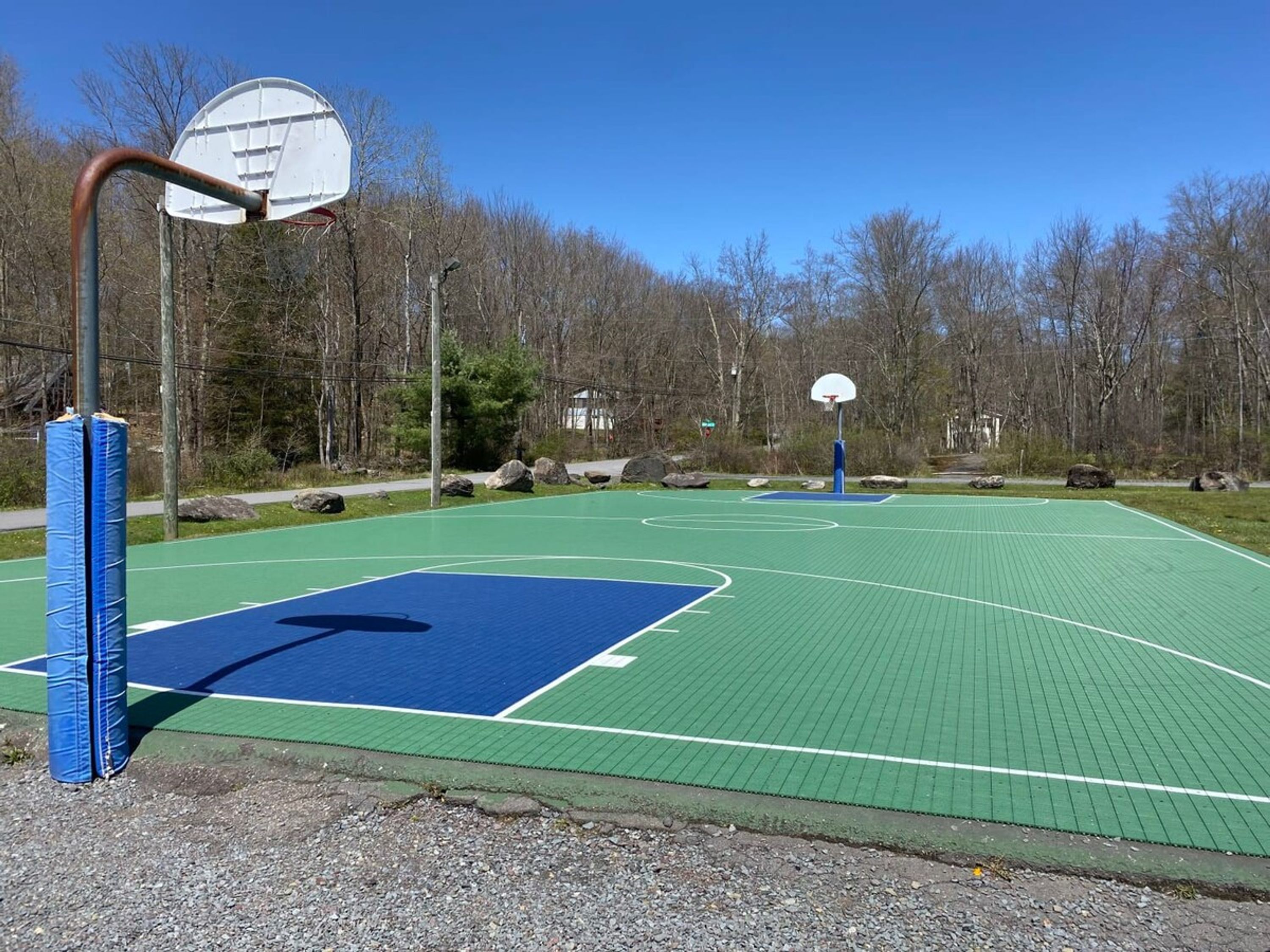 An outdoor basketball court with two hoops, surrounded by trees and a clear sky.