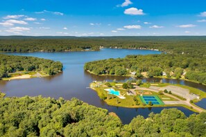 An aerial view of a lake surrounded by dense forest, with a small dock and a tennis court visible. - Cozy Poconos Retreat Hot Tub Dog Friendly Firepit (Pocono Lake)