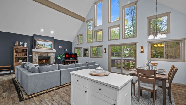 A spacious living room with a fireplace, a dining area, and large windows. - Near Jfbb for Skiing With Hot Tub and Fire Pit (Blakeslee)