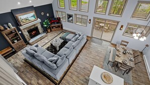 A modern living room with a sectional sofa, fireplace, dining area, and large windows. - Near Jfbb for Skiing With Hot Tub and Fire Pit (Blakeslee)