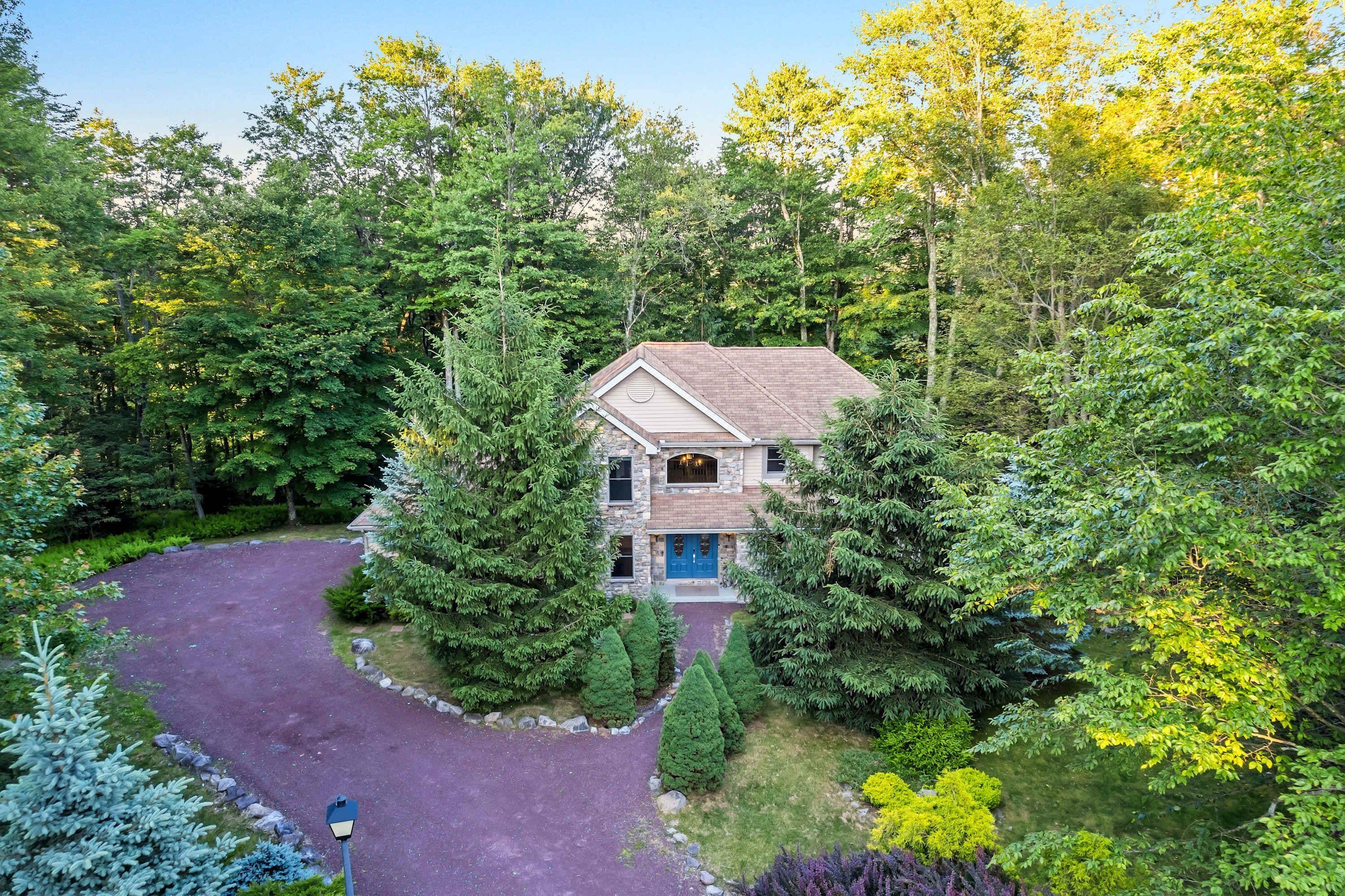 A house surrounded by dense forest, with a driveway leading to the front door.