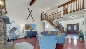 A spacious living room with a staircase, a stone wall, a hanging chair, and a large painting. - Spa Retreat With Hot Tub Sauna and Game Rooms (Lake Harmony)