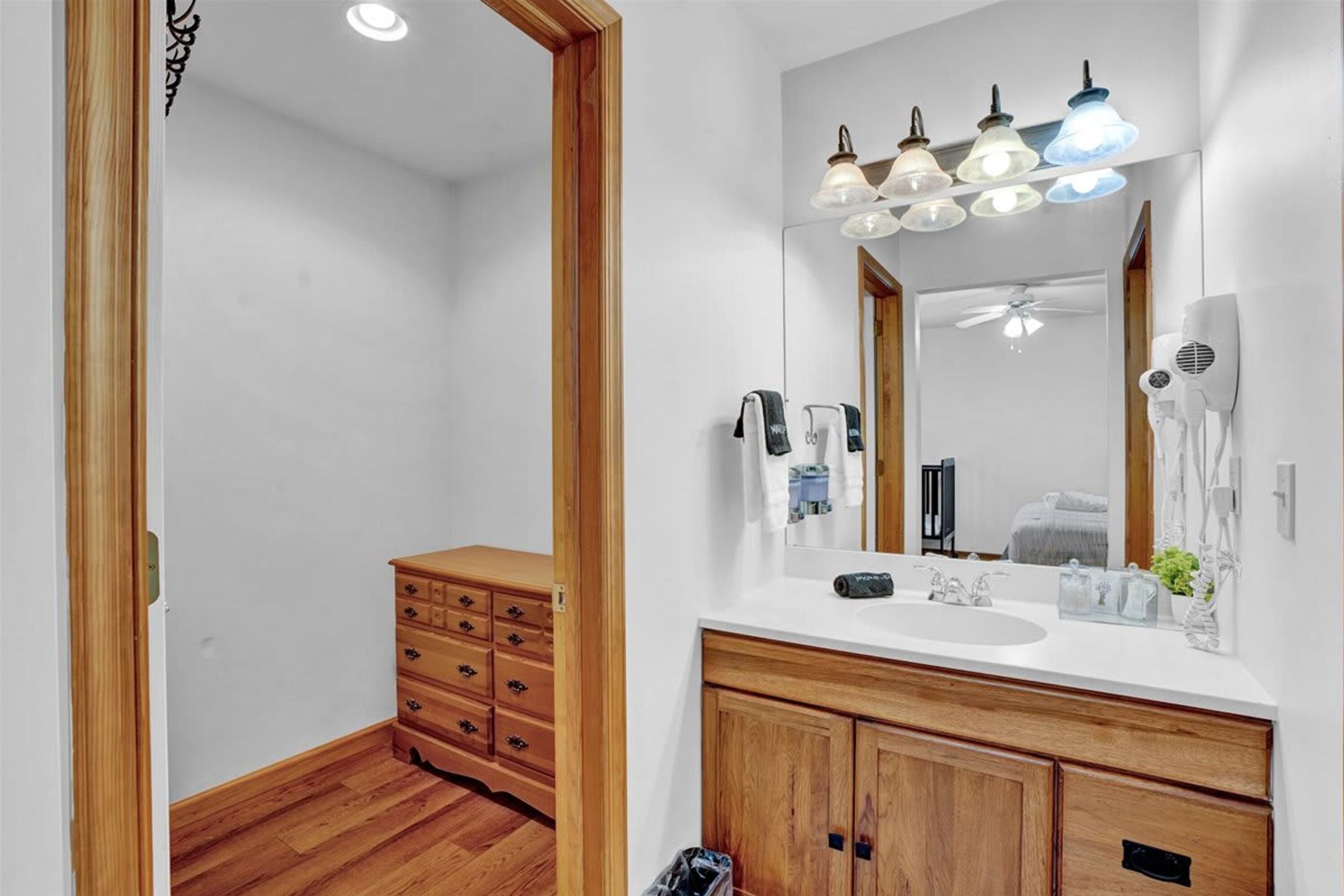A bathroom with wooden cabinets, a white sink, and a mirror with lights above.