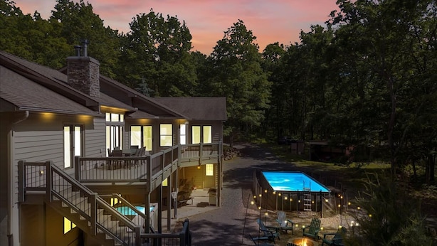Una casa de dos pisos con piscina, mobiliario exterior y una escalera que conduce al nivel superior.