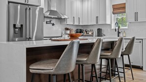 Cozinha moderna com armários brancos, eletrodomésticos de aço inoxidável e uma ilha central com banquetas.