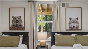 Quarto com duas camas, janela com cortinas, abajur em uma mesa de cabeceira e quadros de animais na parede.