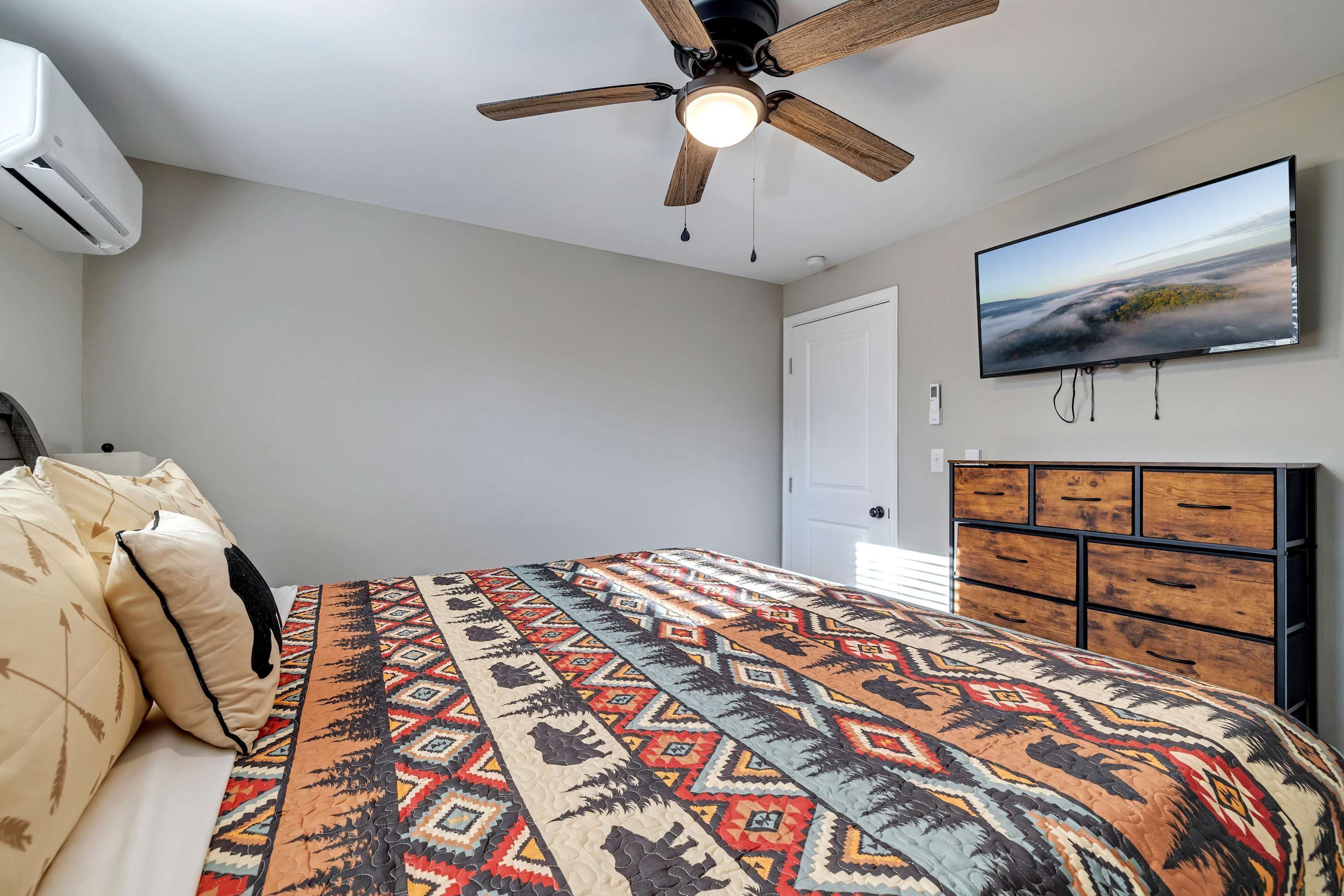 Ein Schlafzimmer mit Bett, Deckenventilator, Fernseher und Kommode.