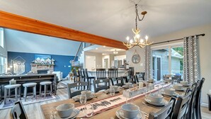 A dining area with a wooden table set for six, surrounded by chairs, a chandelier, and a view of the kitchen and living areas. - Hot Tub Game Room Dog Friendly Sports Bar A C (Albrightsville)